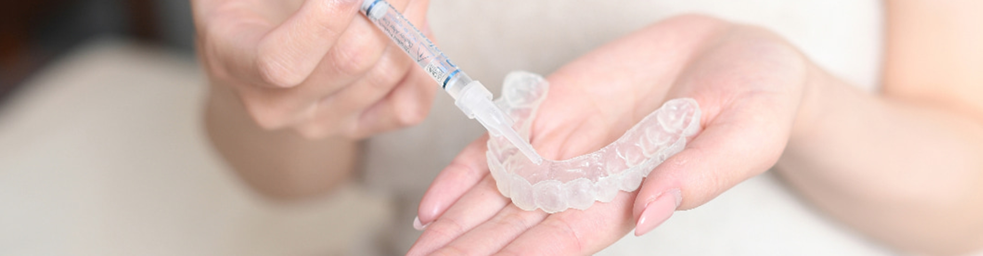 hands injecting whitening gel into clear tray